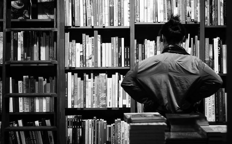 A woman staring at a bookshelf trying to find a book